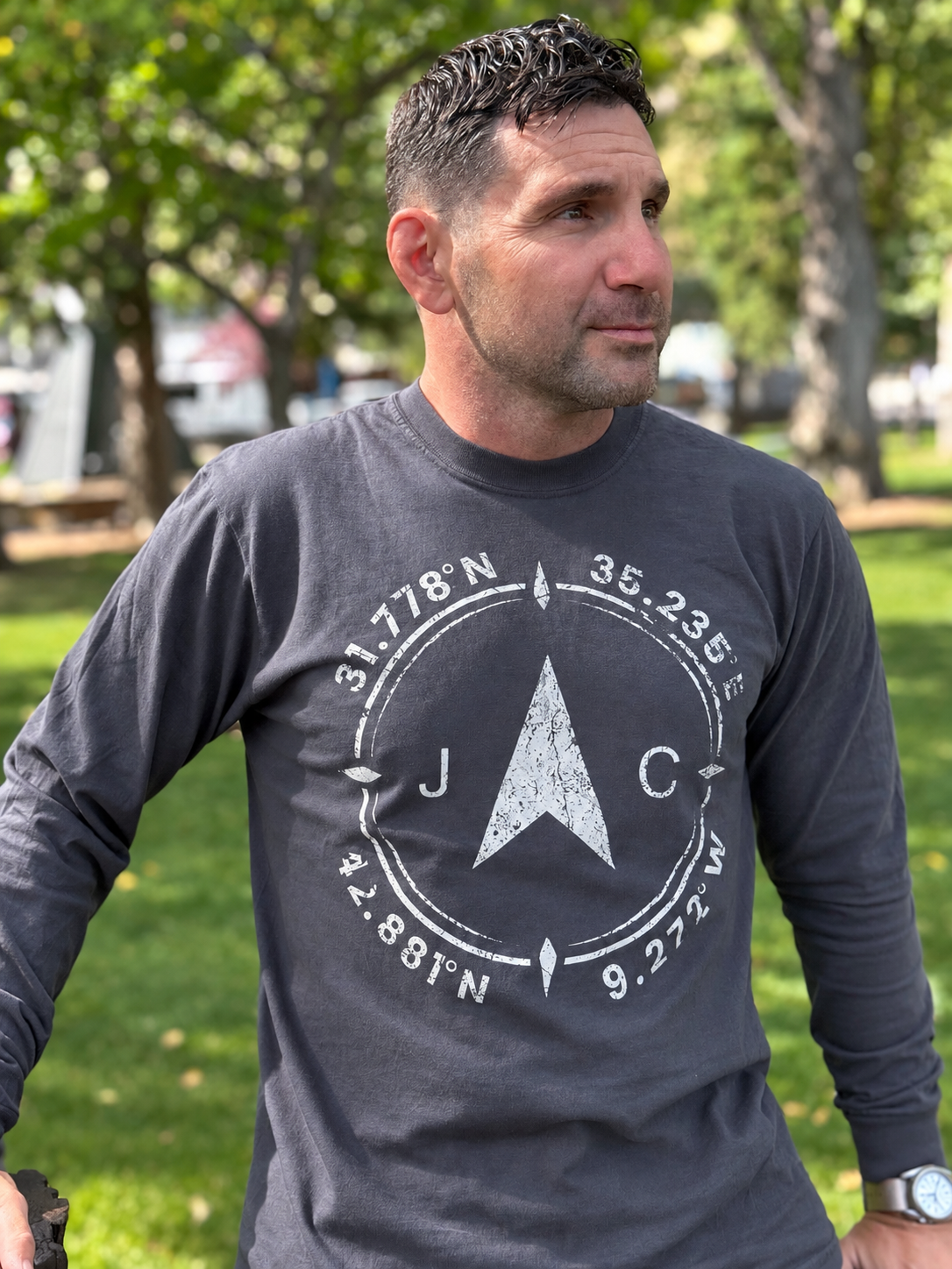 Man wearing the dark Compass long-sleeve with the compass graphic in a sunlit park