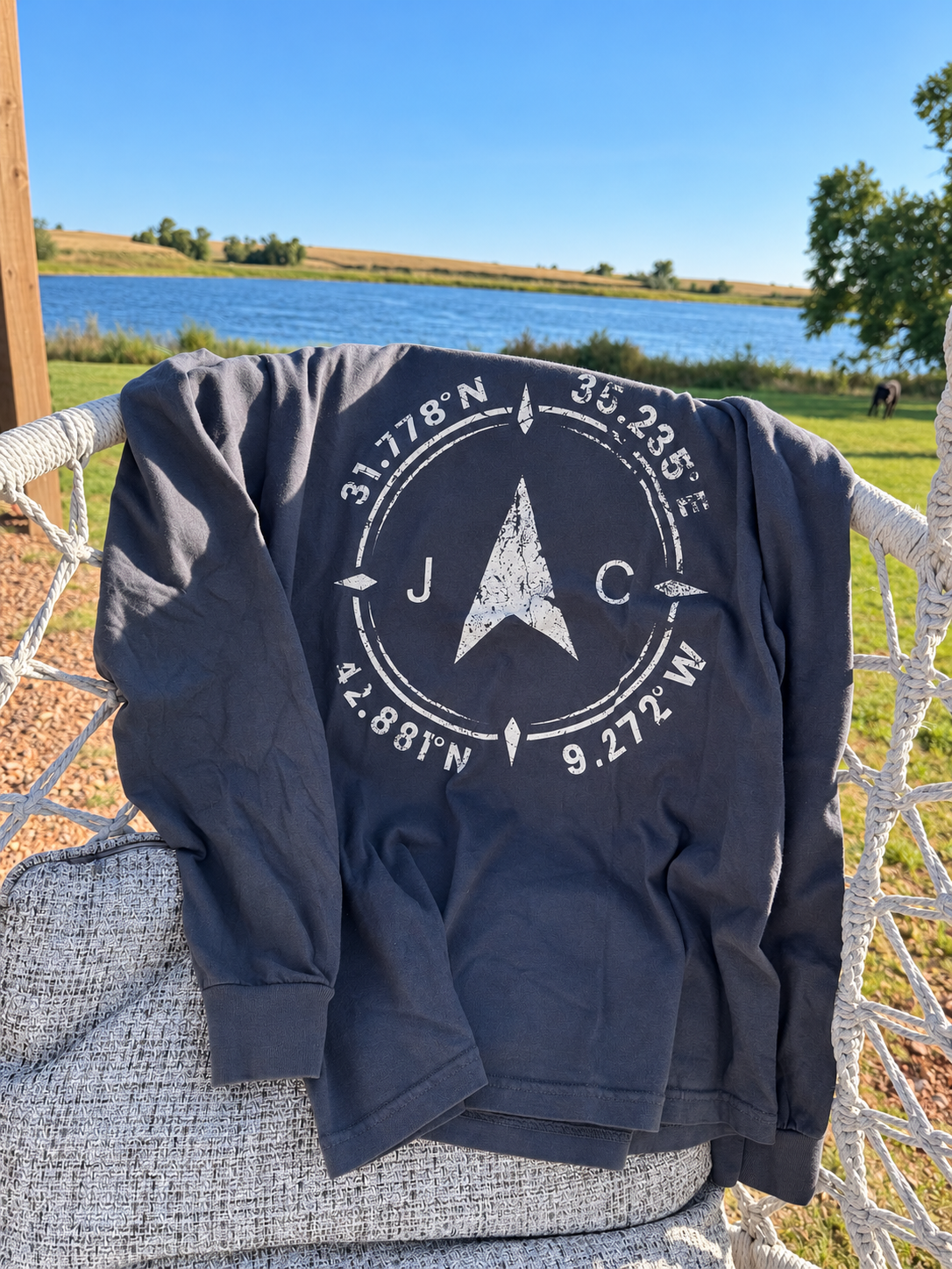 Dark Compass long-sleeve draped over a hammock chair by a lakeside field