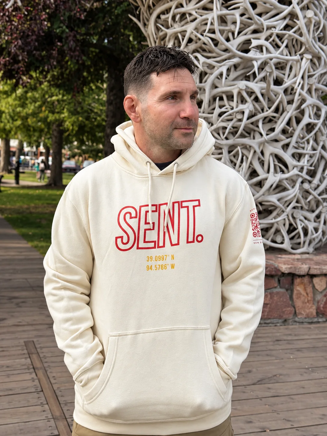 Man wearing a cream SENT. Kansas City hoodie beneath an antler arch