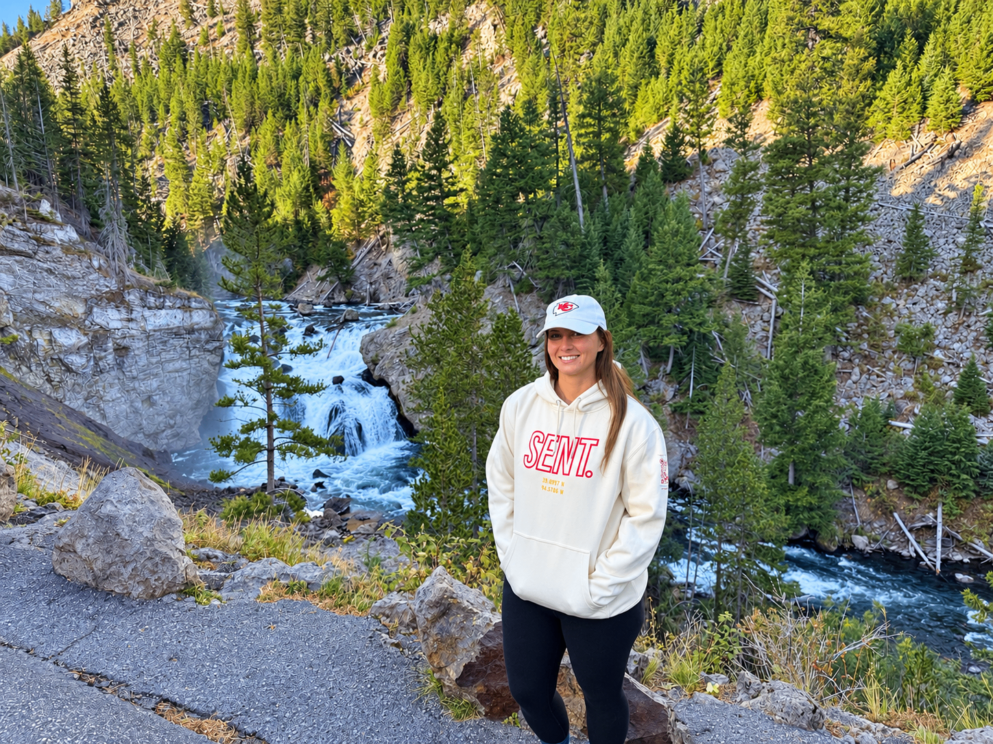 Woman wearing a cream SENT. hoodie above a forest waterfall