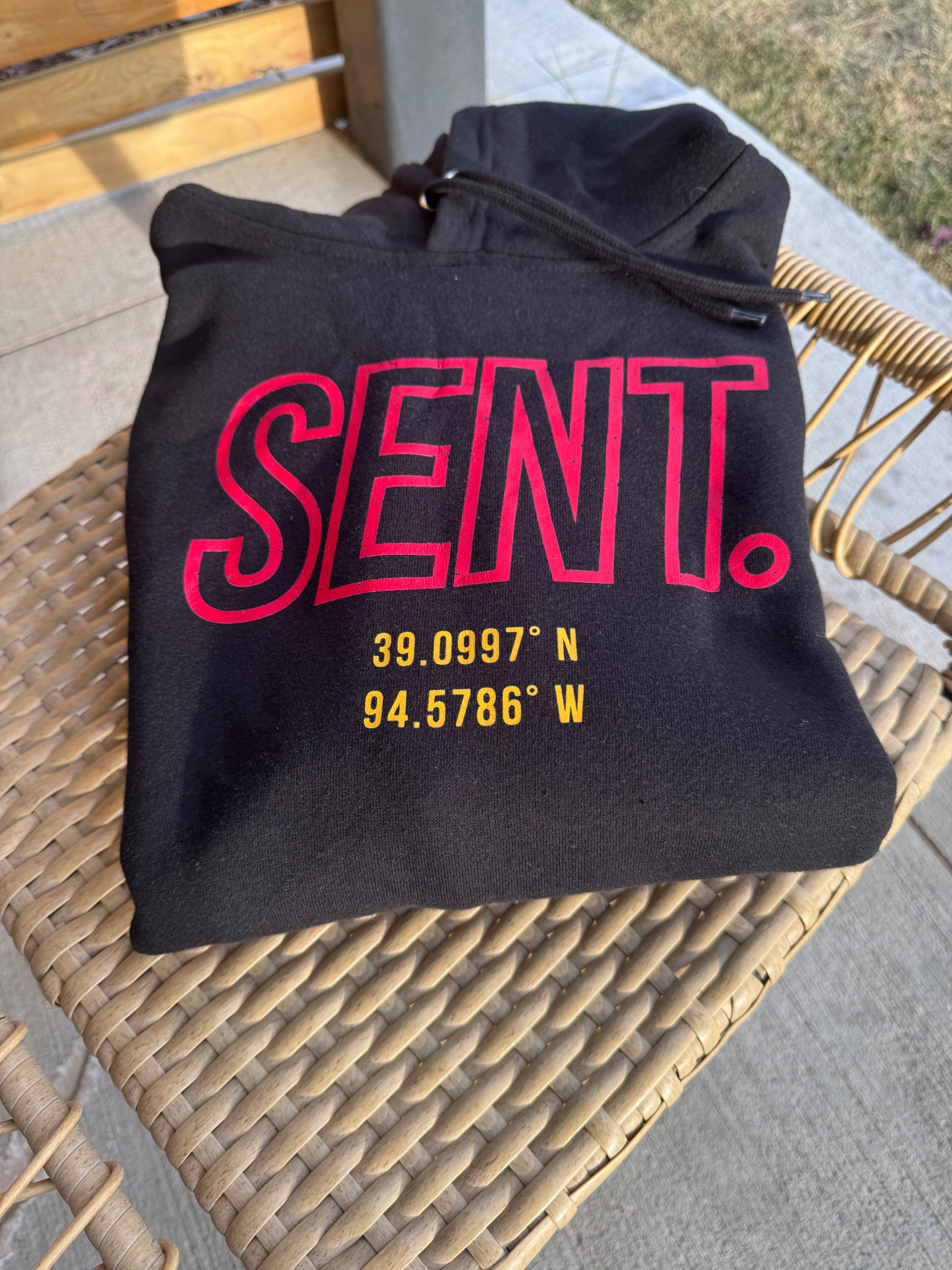 Black KC SENT hoodie laid on a woven chair