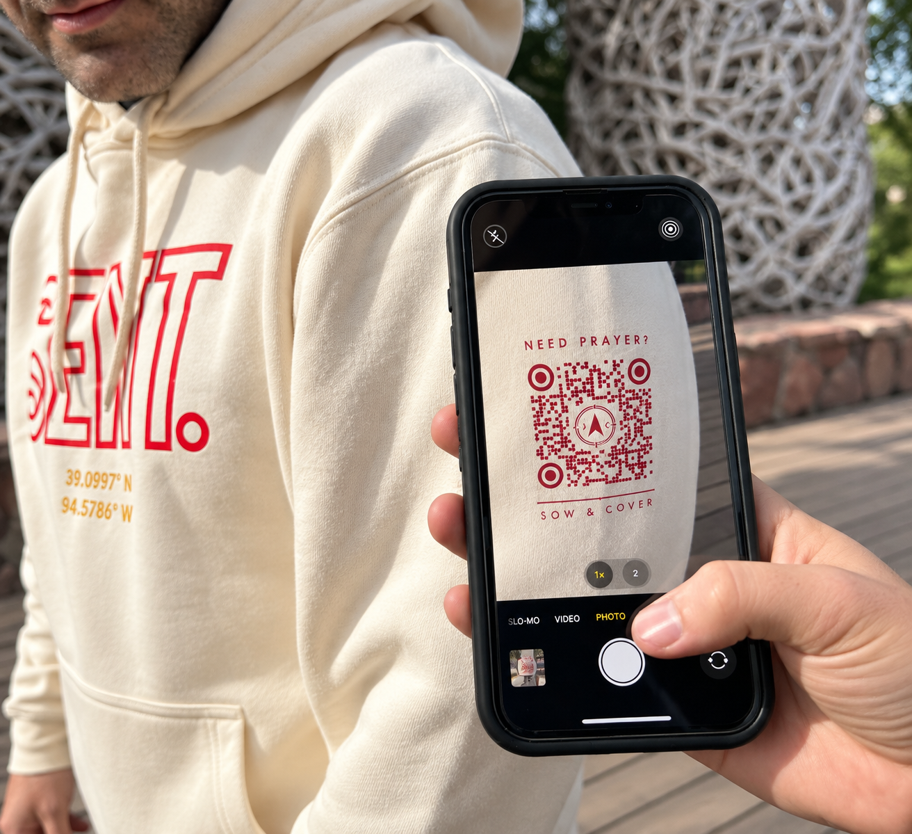 A phone scanning the Need Prayer? QR code on a cream Sow & Cover hoodie